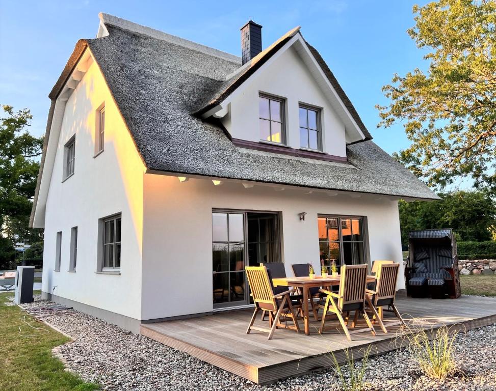 uma casa branca com um deque e cadeiras de madeira em Ferienhaus Svantovit - exklusives Ferienhaus mit Sauna, Whirlpool und Kamin em Putgarten