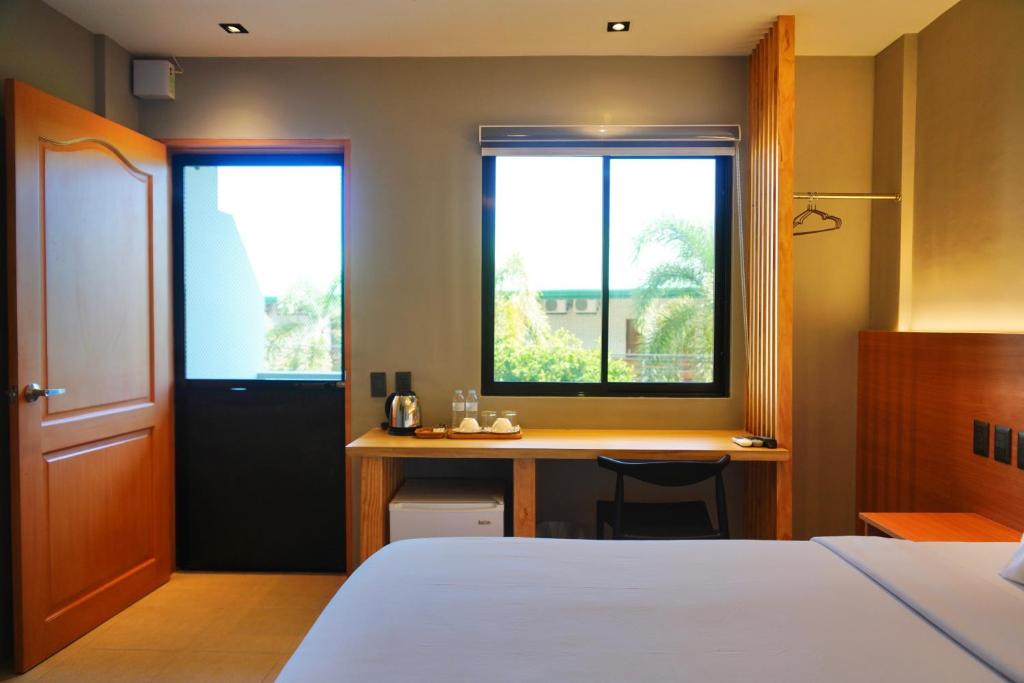 a bedroom with a bed and a desk and two windows at Mayfair Resort in Panglao Island