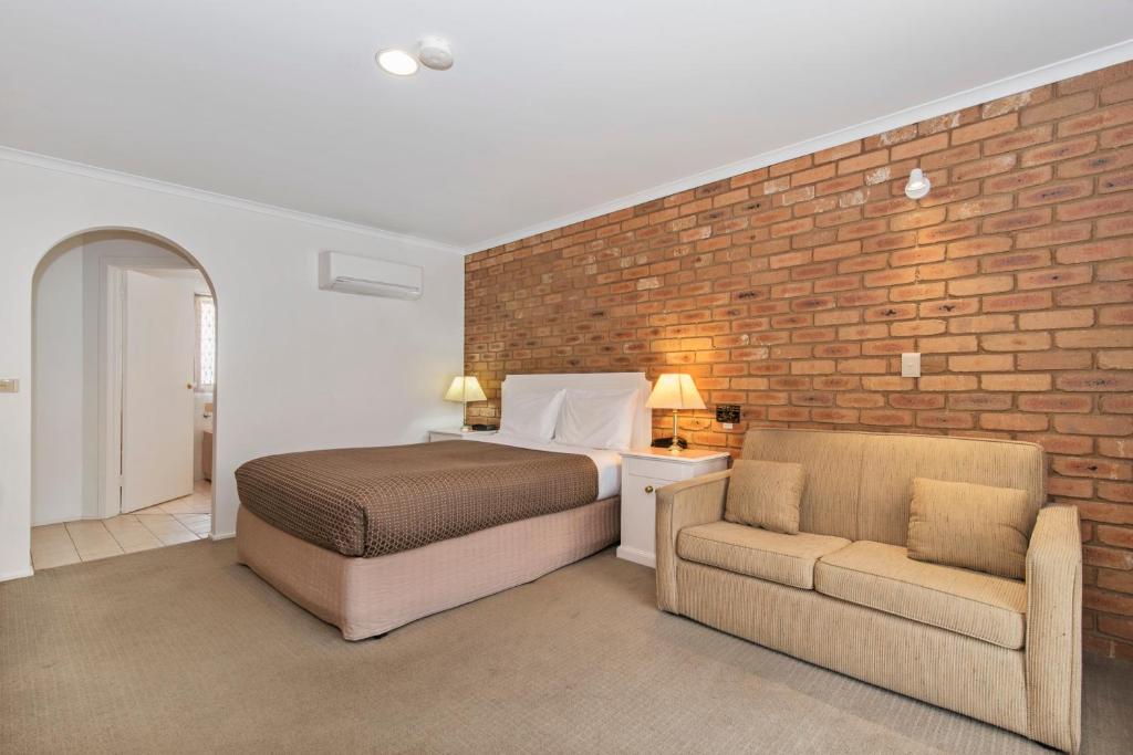 a bedroom with a bed and a chair and a brick wall at Golden Square Motor Inn in Bendigo
