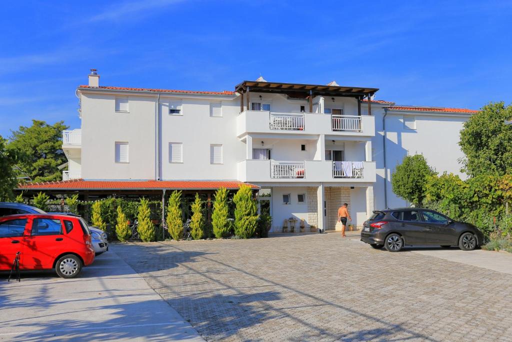 a building with two cars parked in a parking lot at Apartments by the sea Rogoznica - 4162 in Rogoznica