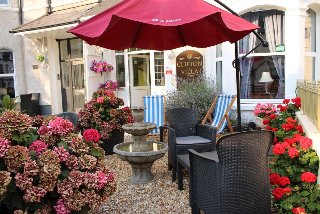 un patio con sillas, sombrilla y flores en Clifton Villa Guest House en Llandudno