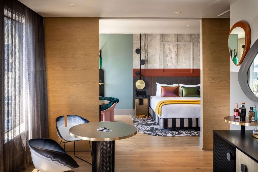QT Auckland في أوكلاند: غرفة فندقية بسرير وطاولة وكراسي