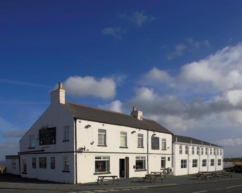 The Brown Horse Hotel في Wolsingham: مبنى أبيض مع طاولات نزهة أمامه