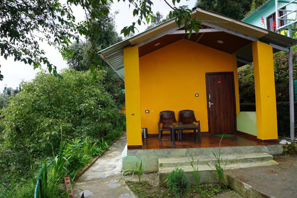 ein gelbes Haus mit zwei Stühlen davor in der Unterkunft DRONA HILLS RESORTS in Kanatal