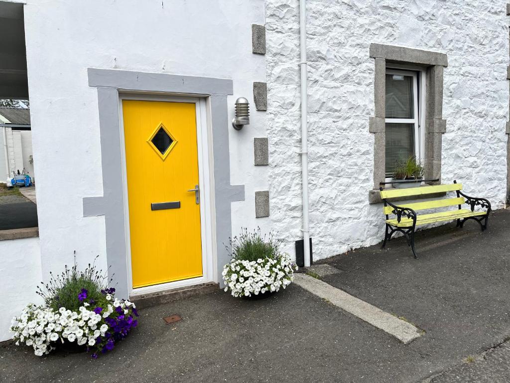 a yellow door on a white building with a bench at St John's Town of Dalry Glentress Apartment 1 in Dalry