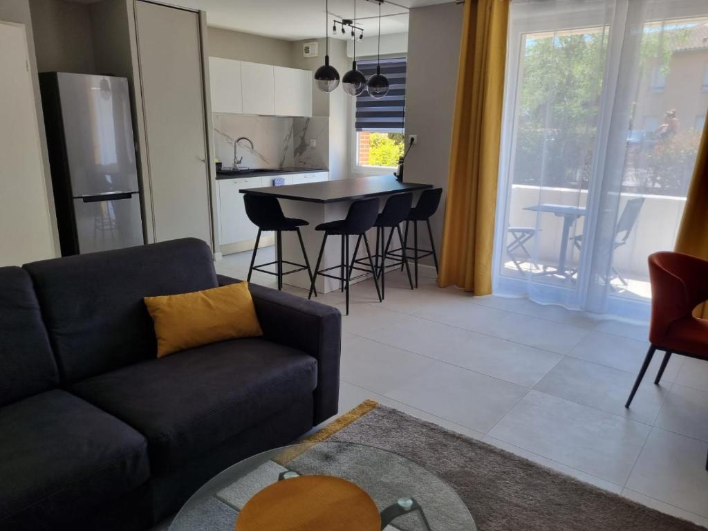 a living room with a couch and a table and a kitchen at LE MONTI appartement proche MEETT, Aéroport Blagnac, Airbus, Golf international de Seilh in Mondonville
