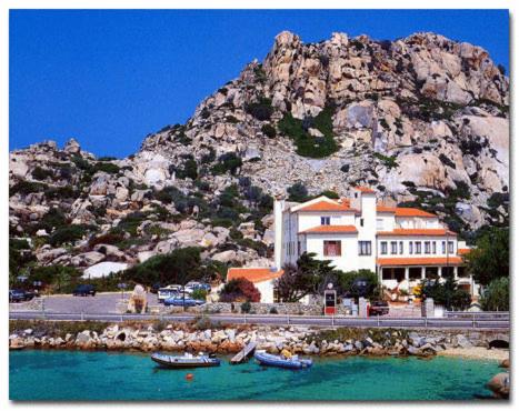 un edificio con barcos en el agua frente a una montaña en Hotel Nido D'aquila, en La Maddalena