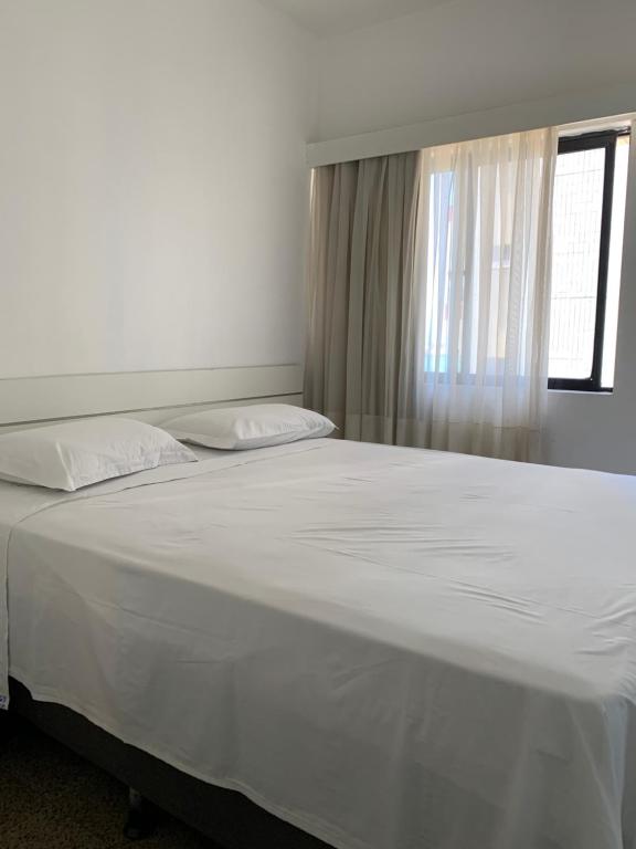 1 cama blanca grande en un dormitorio con ventana en Vila Costeira Flat Apto Particular, en Fortaleza