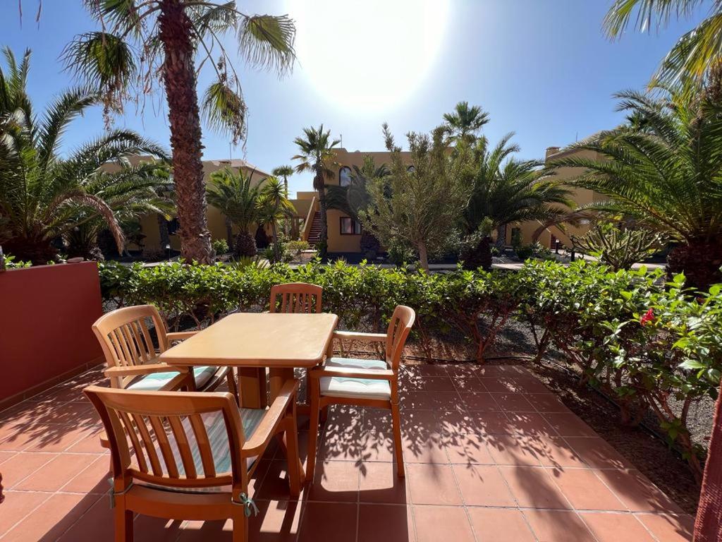 a wooden table and chairs on a patio with palm trees at Corralejo Happy Place, precioso apartamento con piscina in Corralejo