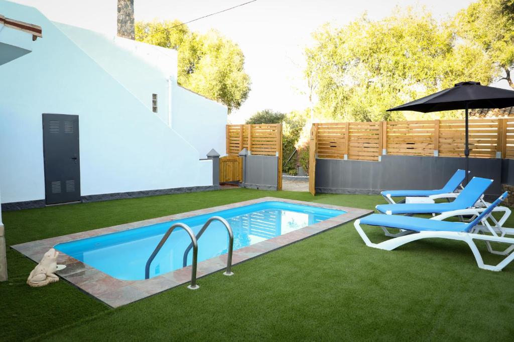 a backyard with a swimming pool with chairs and an umbrella at Casa La Herradura 1 in Vejer de la Frontera