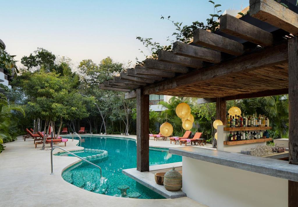 a patio area with a pool, chairs, tables and umbrellas at Kimpton Aluna Resort Tulum, an IHG Hotel in Tulum