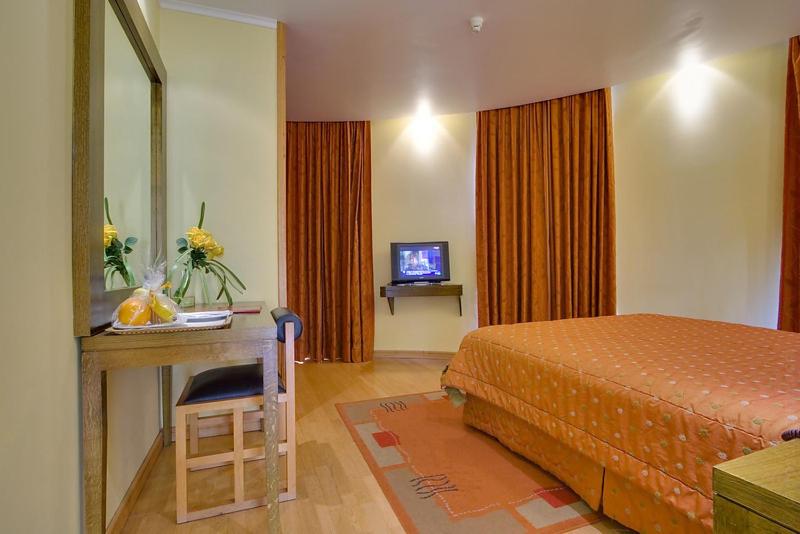 A warmly furnished double room with a desk, mirror, television and patterned curtains.