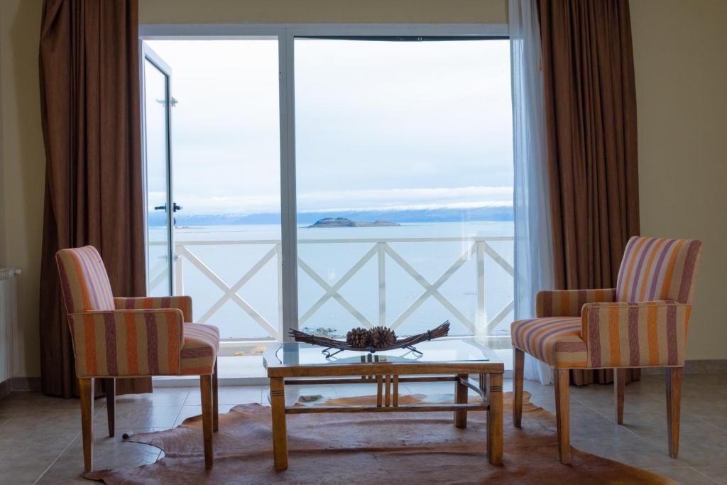 ein Wohnzimmer mit 2 Stühlen, einem Tisch und einem großen Fenster in der Unterkunft Hotel Las Dunas in El Calafate