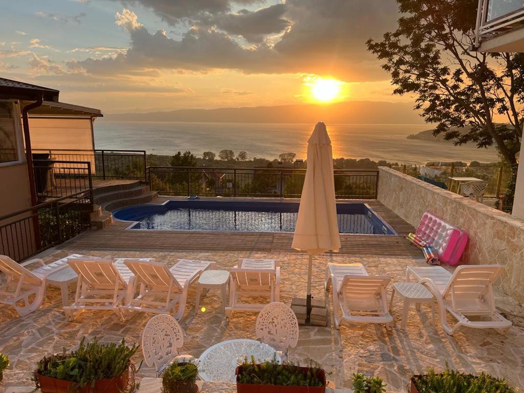 a sunset over a pool with chairs and a umbrella at Villa Aurora in Ohrid