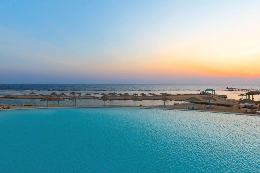 a swimming pool next to the beach at sunset at Radisson Blu Resort El Quseir in Quseir
