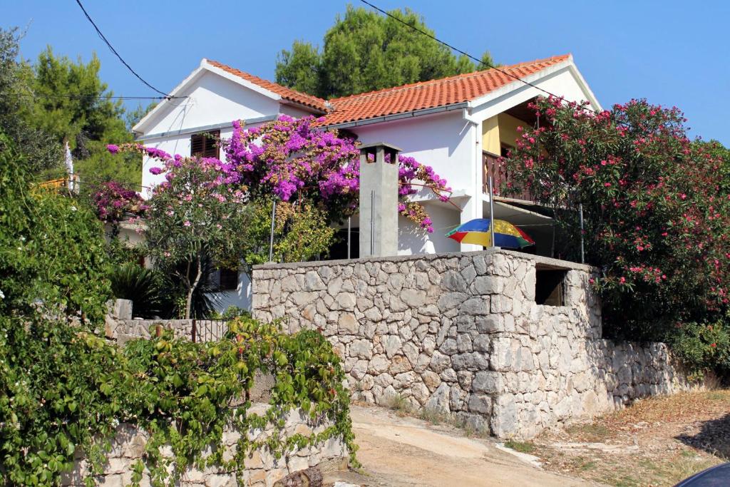 una casa detrás de una pared de piedra con una sombrilla en Apartments by the sea Basina, Hvar - 5700, en Vrboska