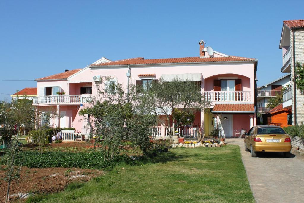 une maison rose avec une voiture garée devant elle dans l&#39;établissement Apartments by the sea Sukosan, Zadar - 5905, à Sukošan