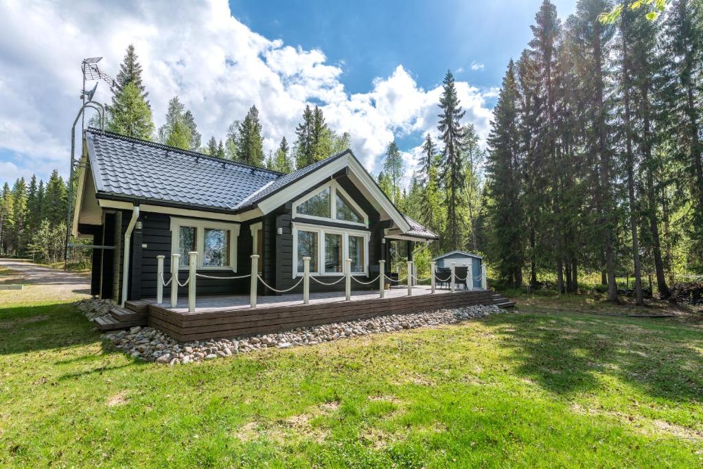 una pequeña casa con una gran terraza en un campo en Lähderinne - Beachfront 2 bedroom log cabin, private beach & sauna en Puolanka