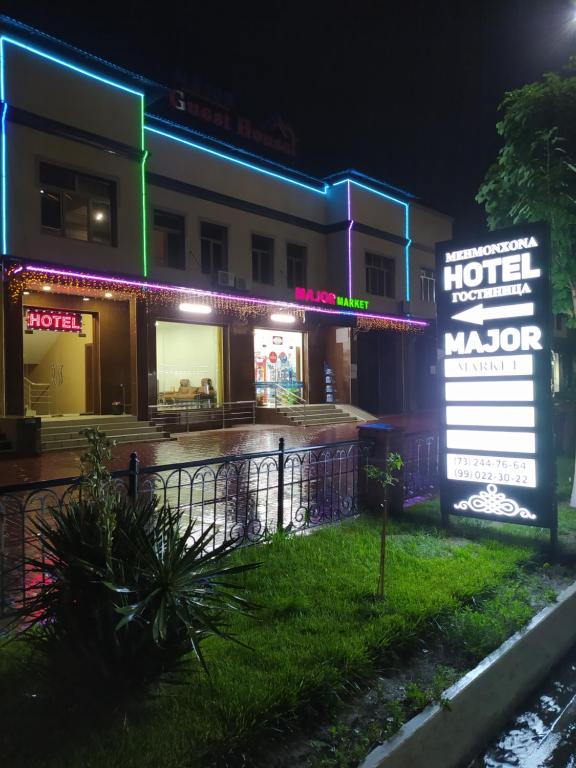 un hotel con un cartel delante de él por la noche en Major Hotel, en Ferganá