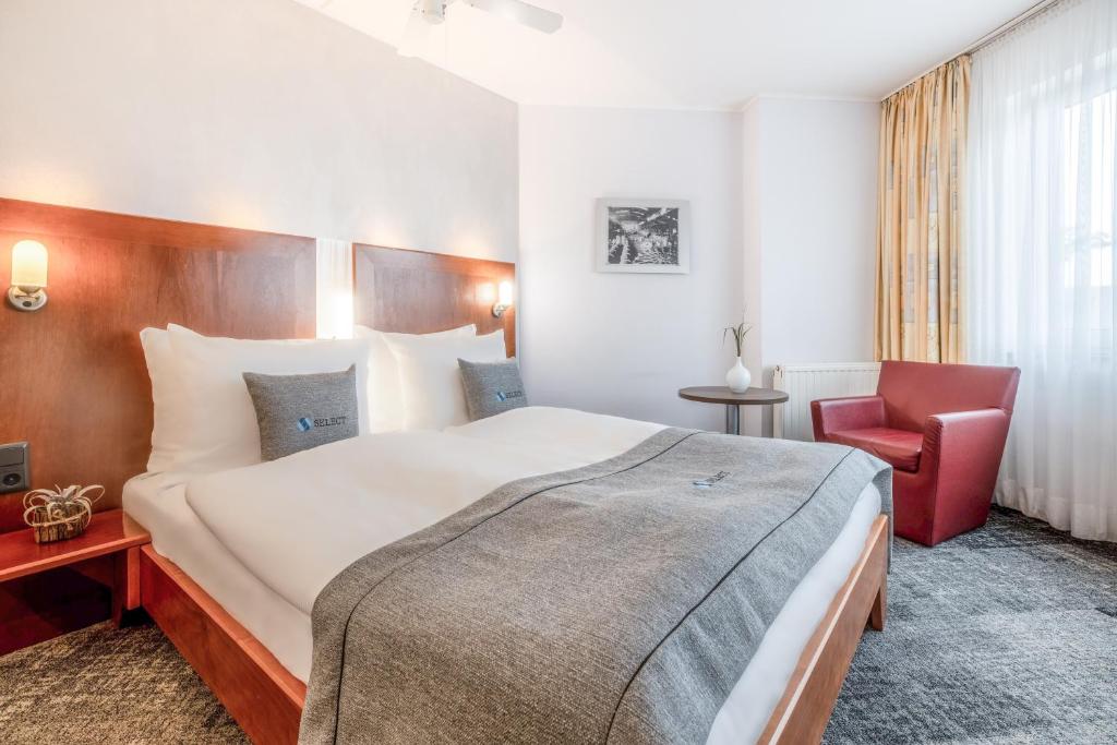 オーバーハウゼンにあるSelect Hotel Oberhausenの大きなベッドと赤い椅子が備わるホテルルームです。