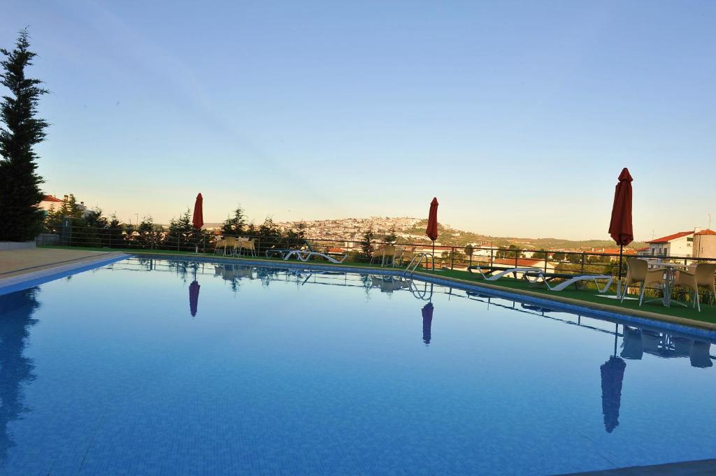 a large swimming pool with blue water and umbrellas at Hotel Lusitania Congress & Spa in Guarda
