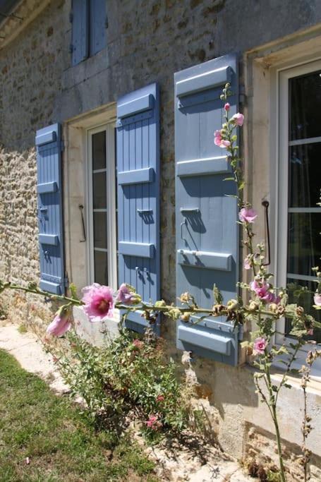 a building with blue shutters and flowers in front of a window at Gîte Rochellier - Charente-Maritime in Cravans