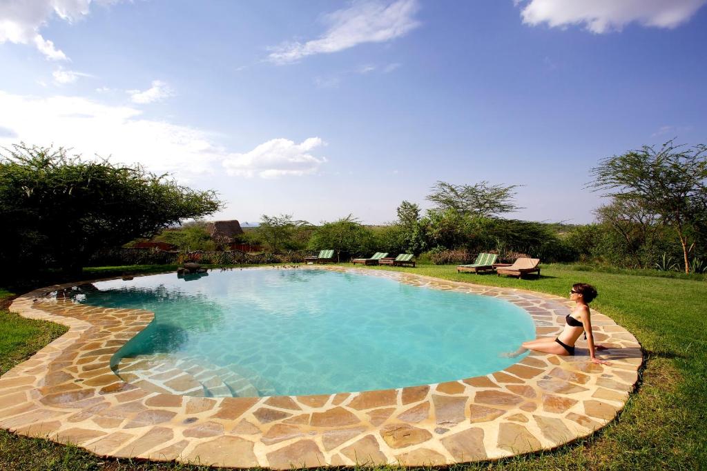 Elewana Lewa Safari Camp في Meru: وجود امرأة جالسة أمام المسبح