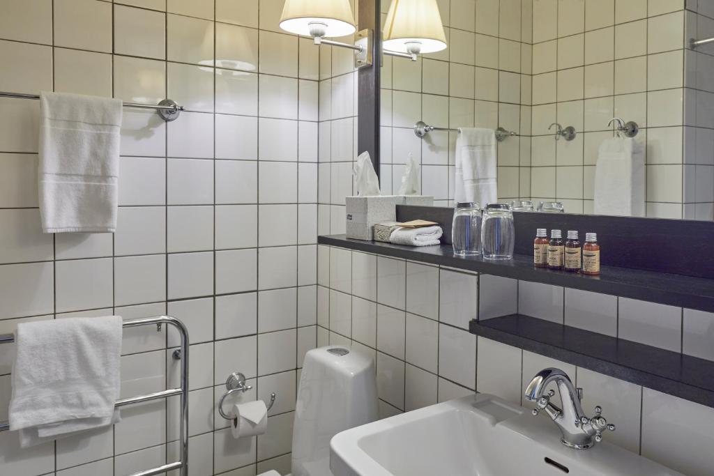a white tiled bathroom with a sink and a mirror at First Hotel Grand in Odense