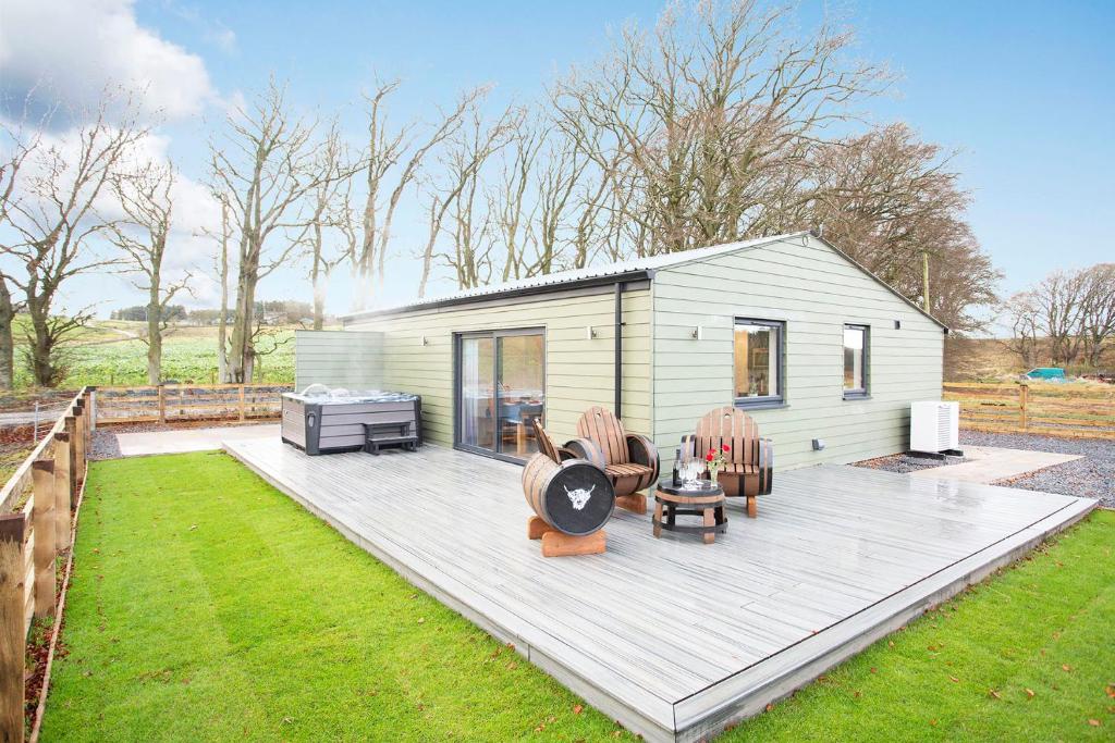 a tiny house with a deck and chairs in a yard at Shiphorns luxury cabin with a hot tub in Eddleston