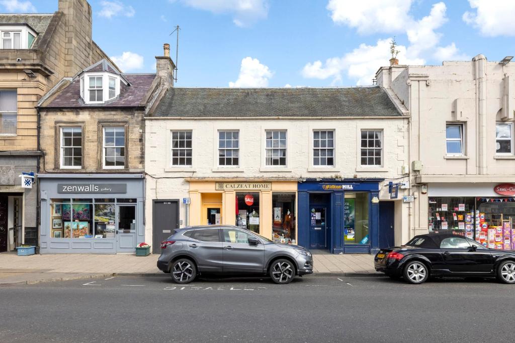 dos coches estacionados en un estacionamiento frente a los edificios en 2 bedroom apartment on Peebles High Street en Peebles