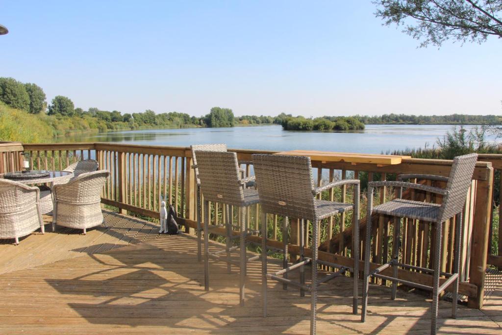 a deck with chairs and a table with a view of a river at Coot Cottage in Somerford Keynes