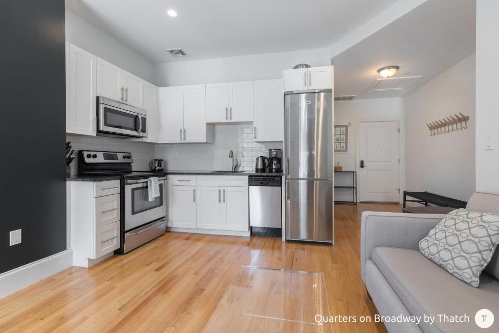 a kitchen with white cabinets and a stainless steel refrigerator at West Broadway Quarters by Thatch in Boston