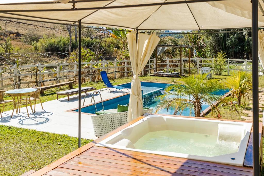 a hot tub with an umbrella next to a pool at Sítio com SPA, lareira e piscina - Piranguinho, MG in Piranguinho