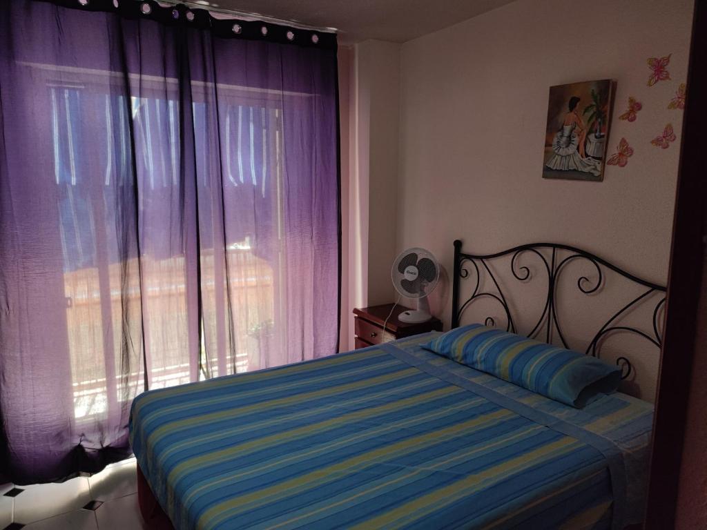 Apartamentos Casa May III - Centro Benidorm في بنيدورم: غرفة نوم مع سرير ونافذة مع ستائر أرجوانية