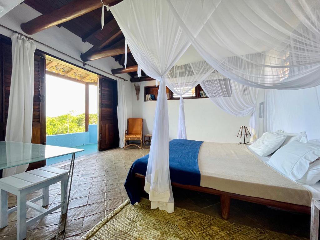 een slaapkamer met een hemelbed en een glazen tafel bij Espelho Bahia Blue House in Praia do Espelho