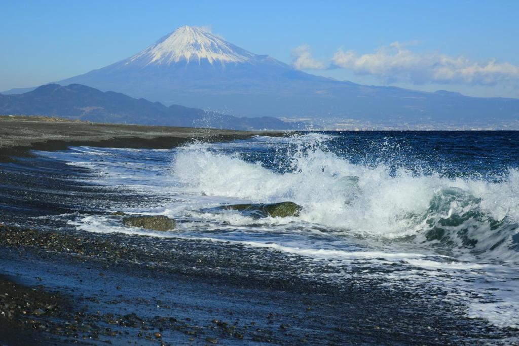 a wave in the ocean with a mountain in the background at Hotel Hagoromo in Shizuoka