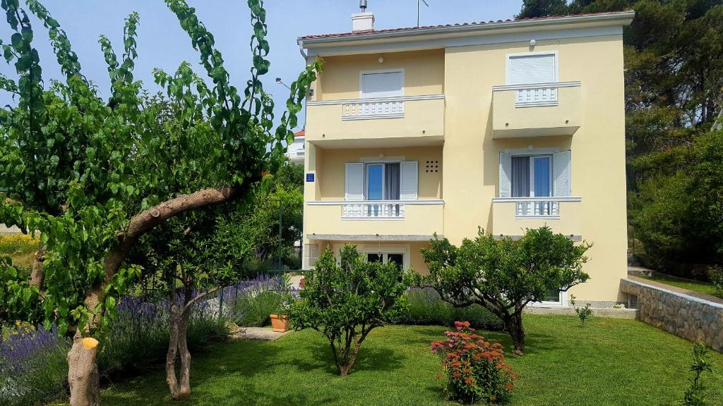 a yellow house with trees and flowers in a yard at Apartments with parking space Rab - 12383 in Rab