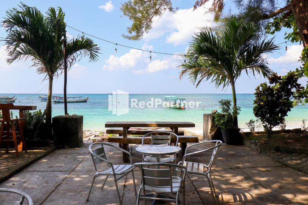 uma mesa e cadeiras com a praia ao fundo em Sahabat Pantai Guest House Mitra RedDoorz em Tanjungbinga