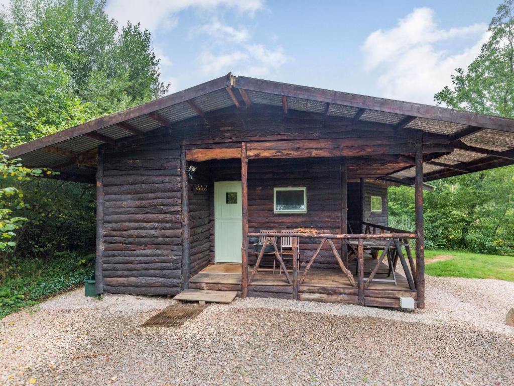 uma cabana de madeira com um alpendre e uma porta branca em The Log Cabin em Honiton