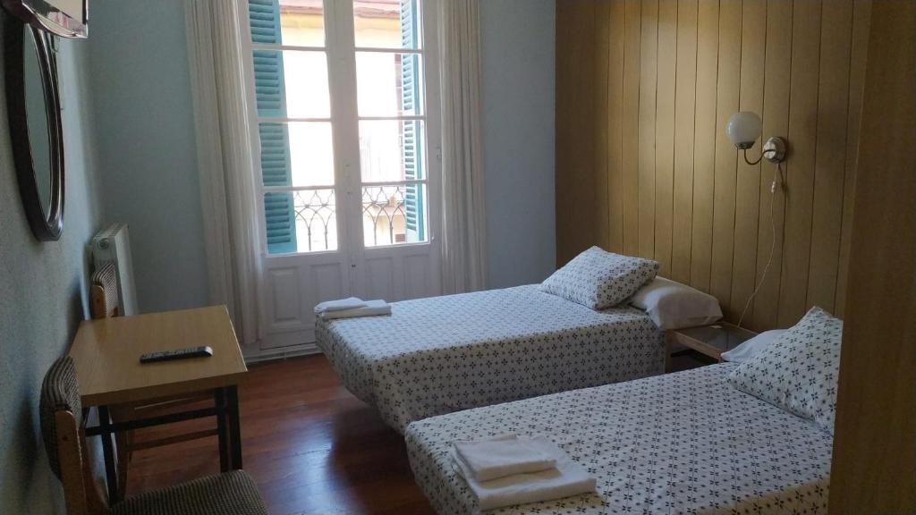 Habitación con 2 camas, mesa y ventana en Pensión Manoli, en Bilbao