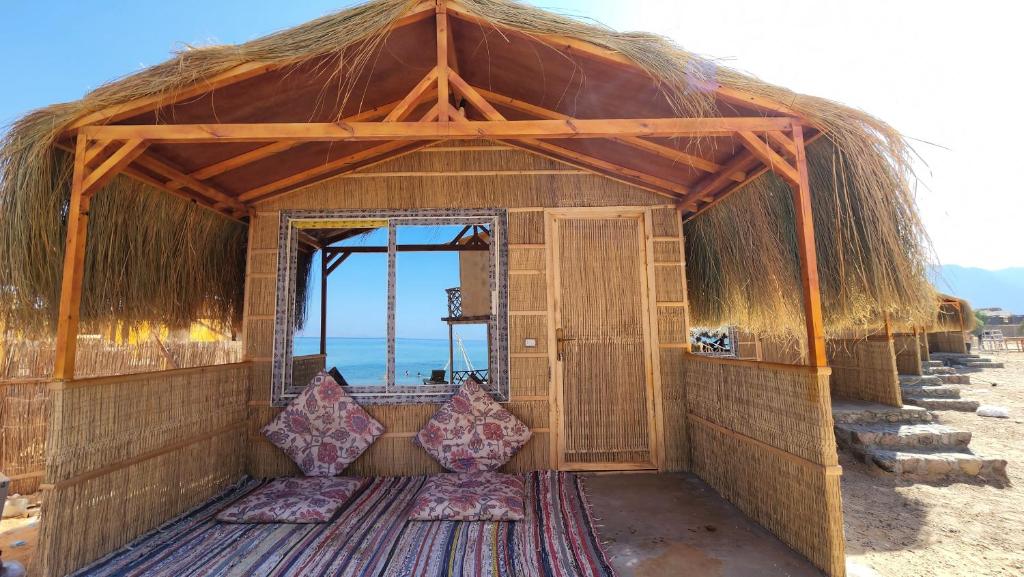 eine kleine Hütte mit einem Strohdach am Strand in der Unterkunft Cinderella Camp Nuweiba in Nuweiba