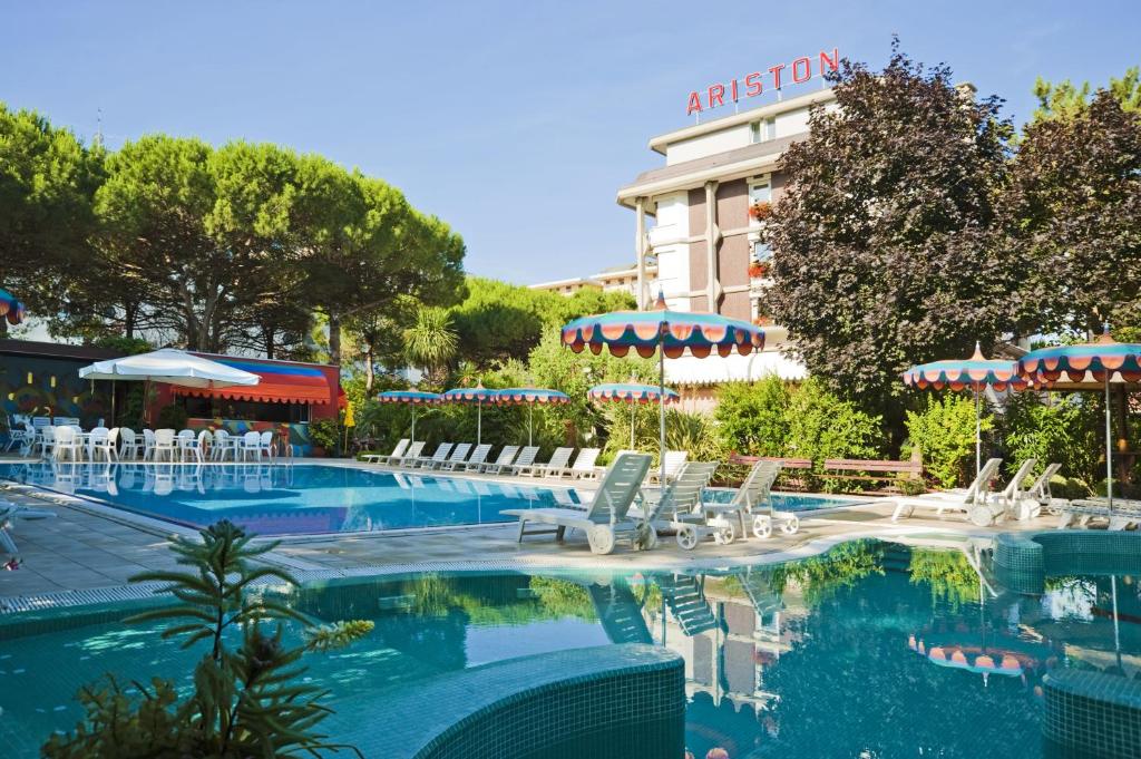 a swimming pool with white chairs and a hotel at Hotel Ariston in Bibione