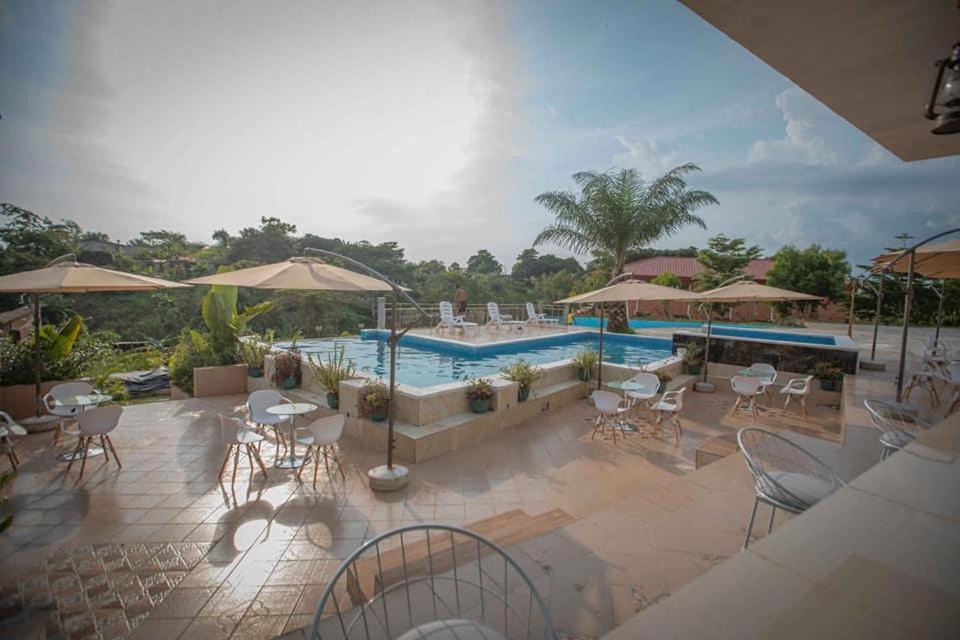 eine Terrasse mit einem Pool, Tischen und Stühlen in der Unterkunft Mont Bleu Hôtel in Assougoula Emo