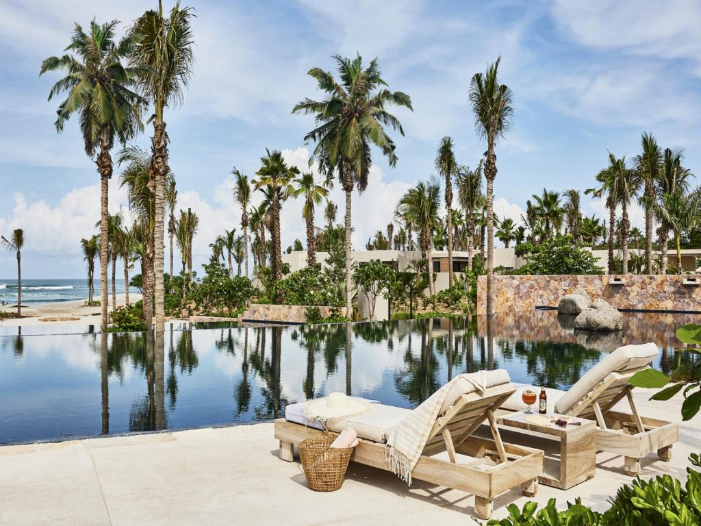 a resort pool with two lounge chairs and palm trees at Susurros del Corazón, Auberge Resorts Collection in Cruz de Huanacaxtle