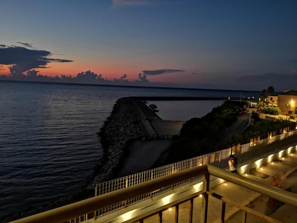 una persona parada en una cerca cerca del agua por la noche en Finestra sul Mare di Alessandro, en Balestrate