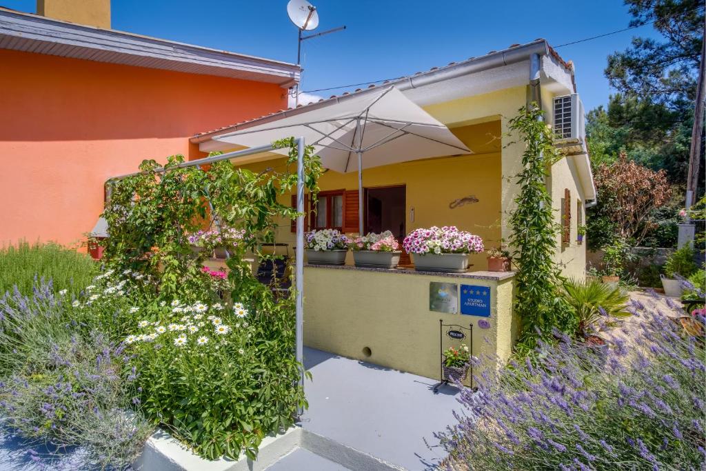 a yellow house with plants and an umbrella at Apartments by the sea Artatore, Losinj - 7952 in Čunski