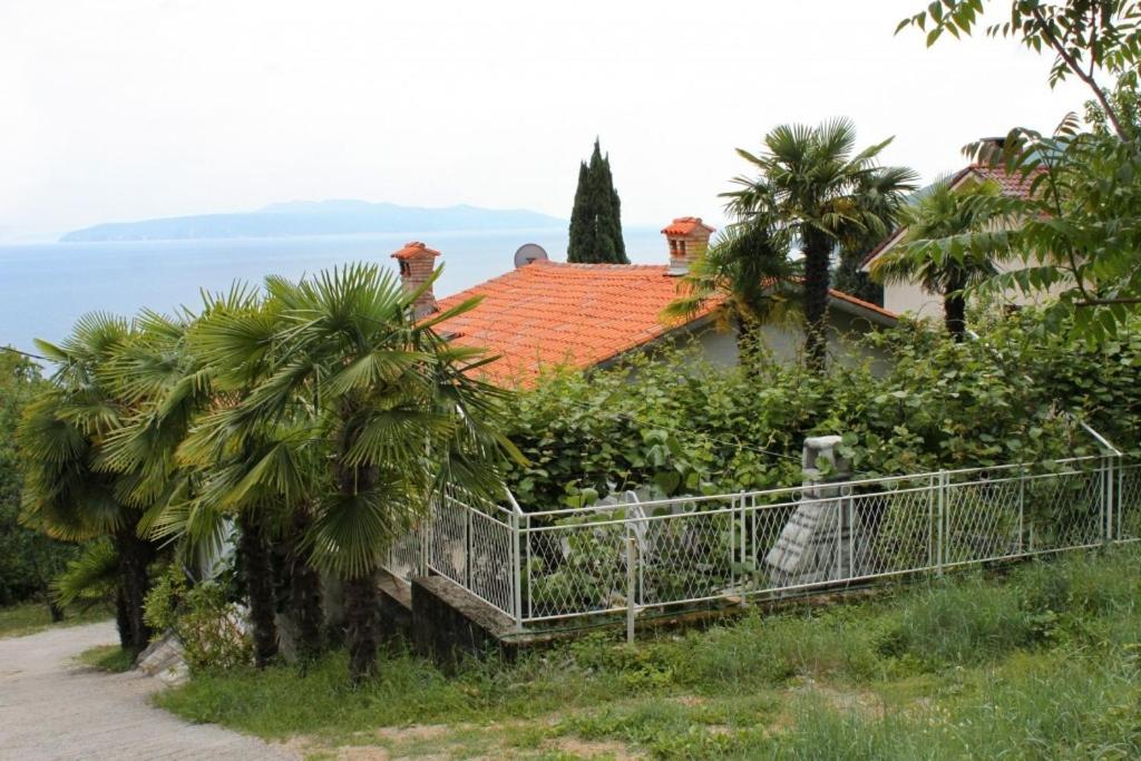 a house with a fence and palm trees and the ocean at Apartments with a parking space Icici, Opatija - 7822 in Ičići