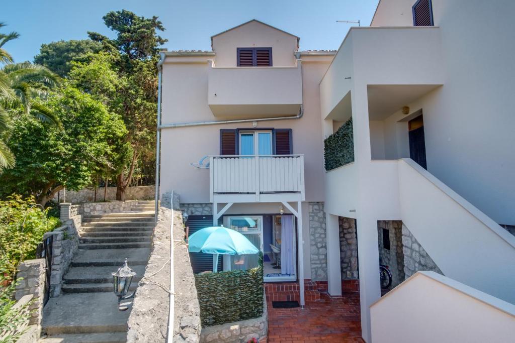 a white house with stairs and a blue umbrella at Apartments with a parking space Mali Losinj (Losinj) - 8067 in Mali Lošinj