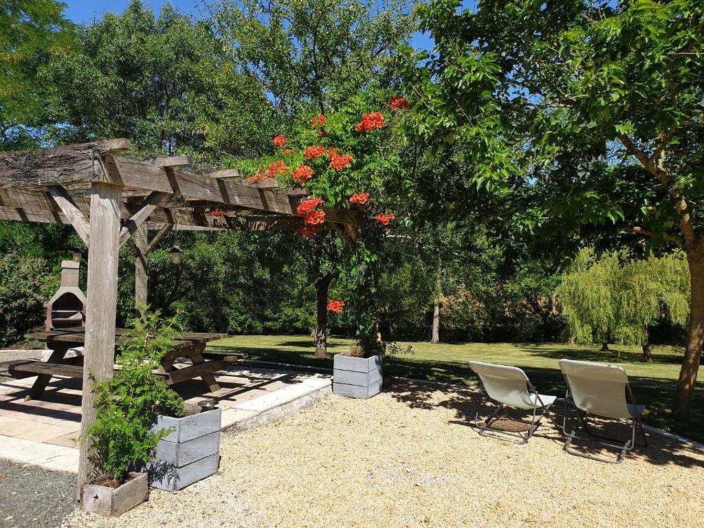 une pergola en bois avec des chaises et une table avec des fleurs rouges dans l'établissement La petite maison de Léo, à Frontenay-Rohan-Rohan