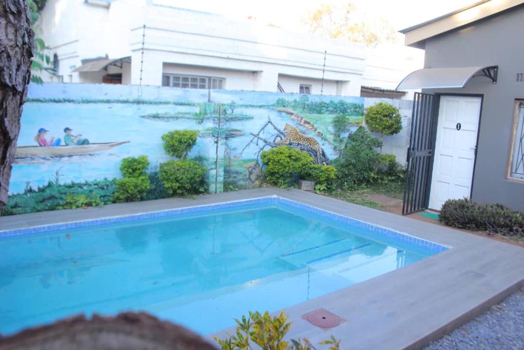 a swimming pool in front of a wall with a mural at Universe GuestHouse in Kasane